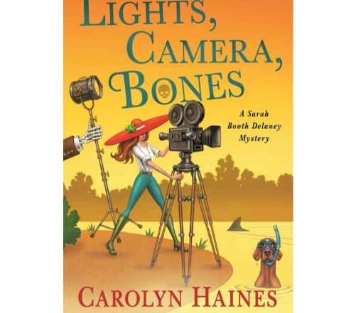 The cover of Lights, Camera, Bones by Carolyn Haines is an illustration of a woman in a big red hat operating a reel-to-reel camera, a skeleton hand holding a stage light, and a dog wearing a snorkel mask